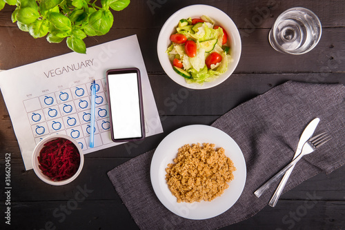 Top view vegetarian and vegan food eating. Healthy dishes - quinoa, fresh vegatable and beetroot salads and dailly veginuary calendar with smartphone on served black wooden table. Day diet planning. photo