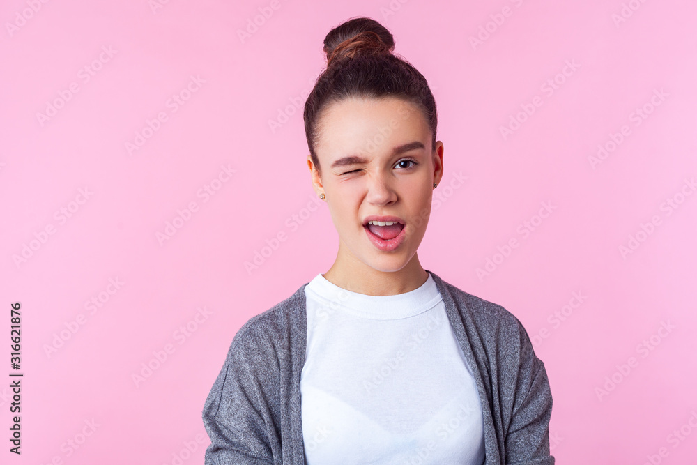 Portrait of playful brunette teenage girl with bun hairstyle in casual clothes winking at camera, looking charming and coquettish, saying hey there. indoor studio shot isolated on pink background Portrait of playful brunette teenage girl with bun hairstyle in casual clothes winking at camera, looking charming and coquettish, saying hey there. indoor studio shot isolated on pink background