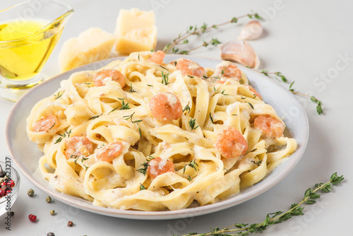 Italian pasta fettuccine or tagliatelle in a creamy sauce with shrimps in a plate on white marble table