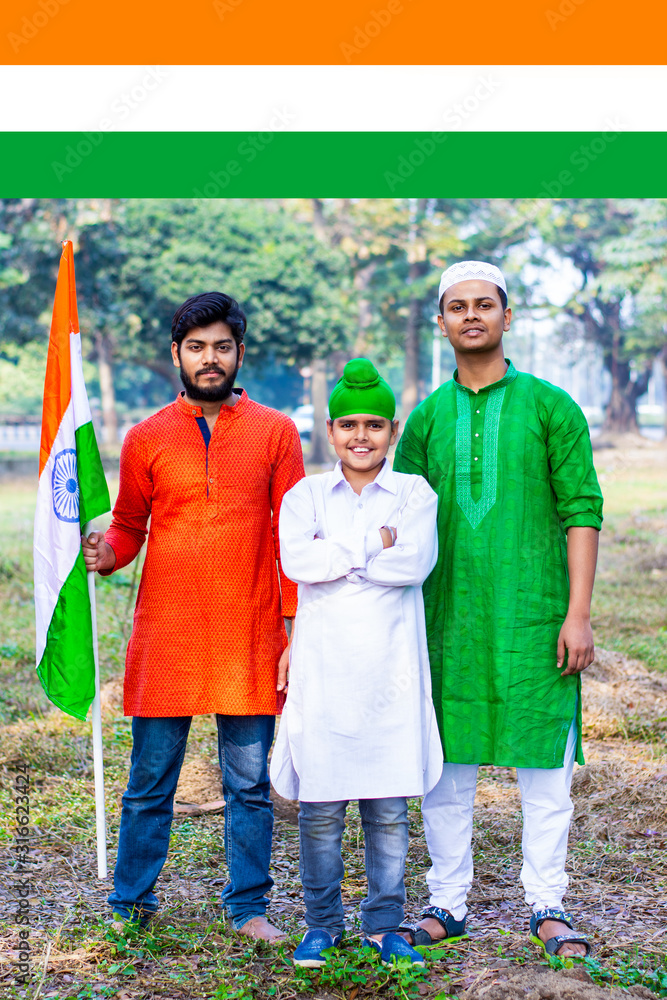 Three kids and young boys of different age and different religion hearing tricolor dress and holding Indian National flag. Indian kids celebrating Republic or Independence day of India. 
