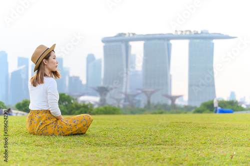 Canvas Print Young asian woman sitting at Marina park against Marina bay in background in vac