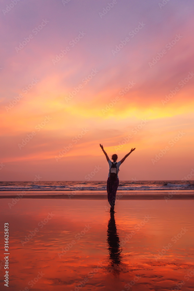 Woman with raised hands feel freedom and enjoying Goa sunset