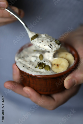 Male hands hold a bowl of yogurt. A man with a spoon eats yogurt with seeds. Chia pudding with pumpkin seeds and banana. Healthy breakfast or snack. Keto diet. Keto dessert. Sugar free dessert
