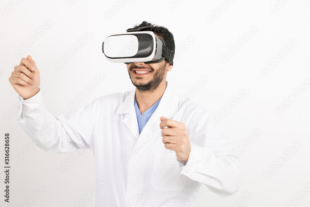 Young smiling male doctor in whitecoat and vr headset standing in isolation