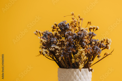 Fototapeta Naklejka Na Ścianę i Meble -  Dried wildflowers. Many tiny blue and yellow flowers in a white vase. Bouquet on a yellow background.