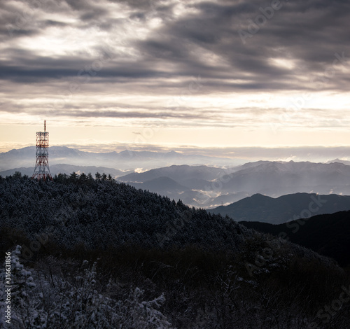 Communication tower on snow covered mountain overlooking misty valley at sunrise