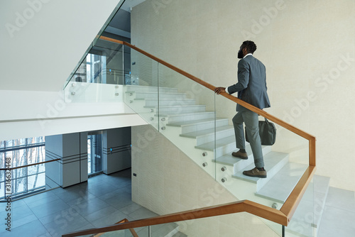 Fotografie Young elegant African businessman with black leather handbag going upstairs