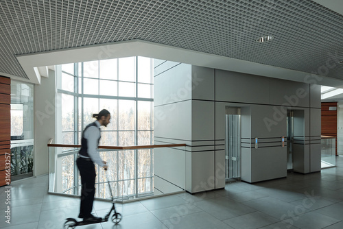 Blurred outline of young businessman moving on scooter in office center