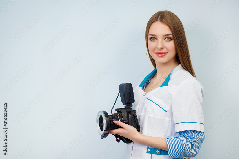 Fototapeta premium Image of a woman doctor isolated over white wall background. Dentist with a camera in hand. Copy space. Beautiful girl in a white coat