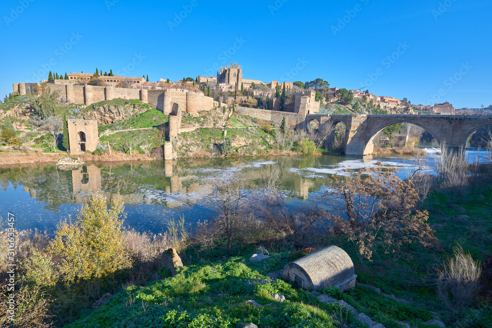 Landscape view of the ramparts, Jewish quarter, San Martin bridge over the Tajo river, Baño de la Cava and  San Juan de los Reyes Monastery in the middle ages city of Toledo, Castilla la Mancha, Spain