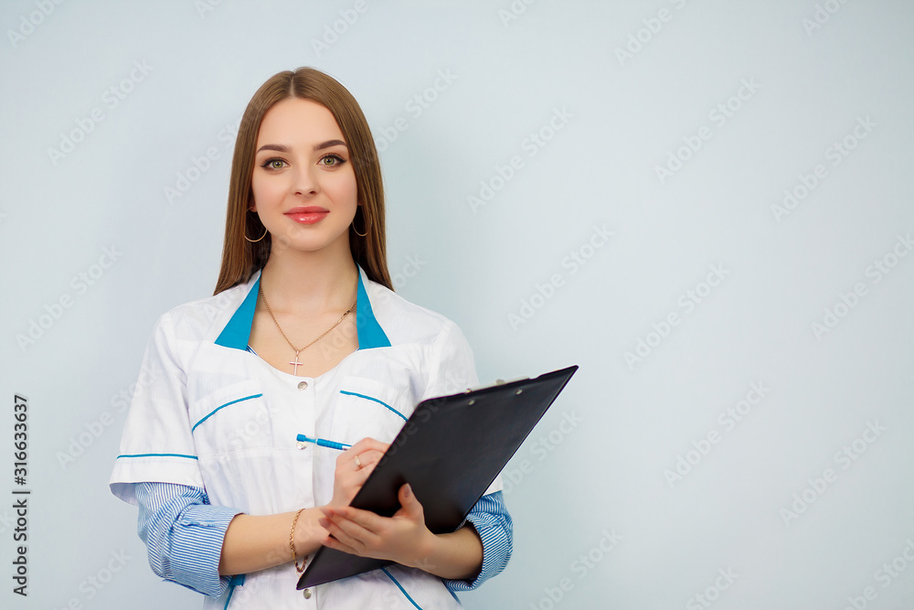 Photo of a young woman doctor posing isolated over white wall background holding clipboard. Health care concept. Beautiful girl in a white coat. Copy space. Photo of a young woman doctor posing isolated over white wall background holding clipboard. Health care concept. Beautiful girl in a white coat. Copy space.