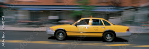 This is a yellow taxi in motion going through Manhattan during the day. The taxi is slightly blurred as is the surrounding scenery.