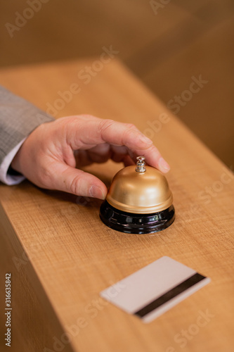 Hand of contemporary businessman over ring button on wooden reception counter