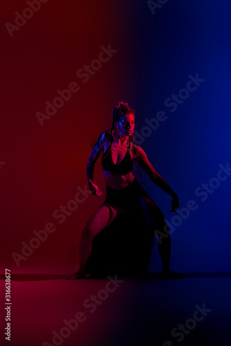 Black dressed and braided hair woman dancing on a blue and red background.