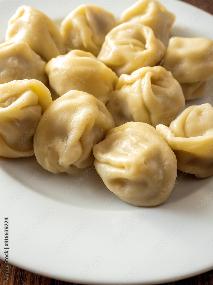 Portion of traditional Russian cooked dumplings on a white plate and wooden table, Close up.