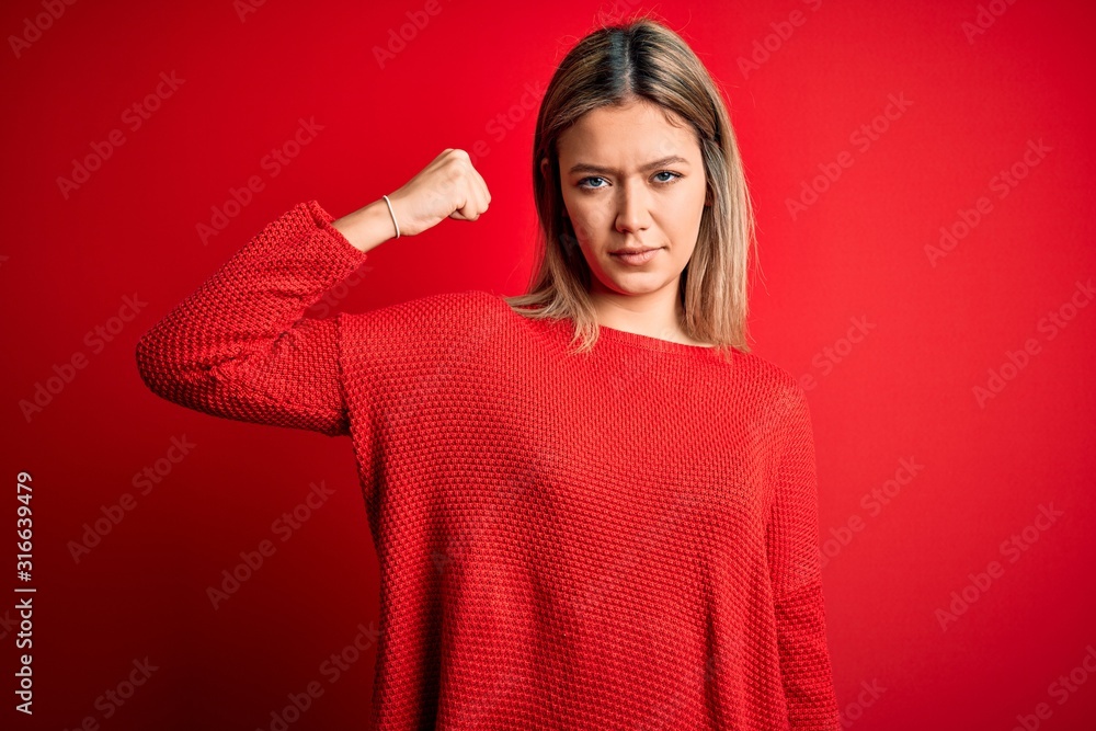 Young beautiful blonde woman wearing casual sweater over red isolated background Strong person showing arm muscle, confident and proud of power Young beautiful blonde woman wearing casual sweater over red isolated background Strong person showing arm muscle, confident and proud of power
