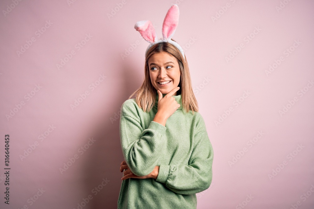 Young beautiful woman wearing easter rabbit ears standing over isolated pink background with hand on chin thinking about question, pensive expression. Smiling with thoughtful face. Doubt concept.