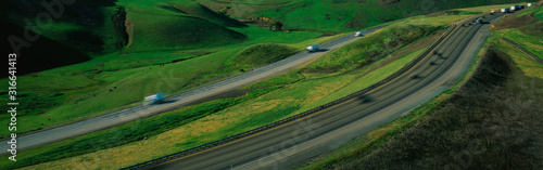 This is Route 580 at the Altamont Pass. There is green grass on each side of the highway with two separate roads for cars to travel in each direction.