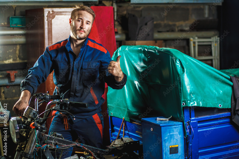 Portrait of a mechanic. A mechanic in a blue protective suit is standing near a moped in a garage. Car service concept. Portrait of a mechanic. A mechanic in a blue protective suit is standing near a moped in a garage. Car service concept.