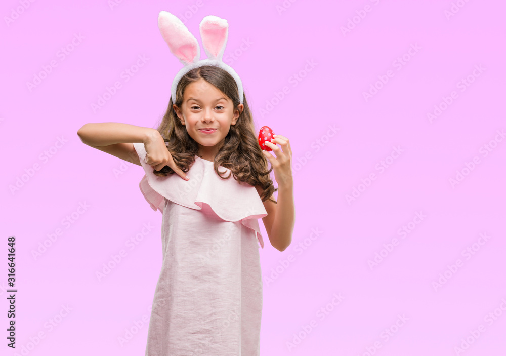 Brunette hispanic girl wearing easter rabbit ears with surprise face pointing finger to himself