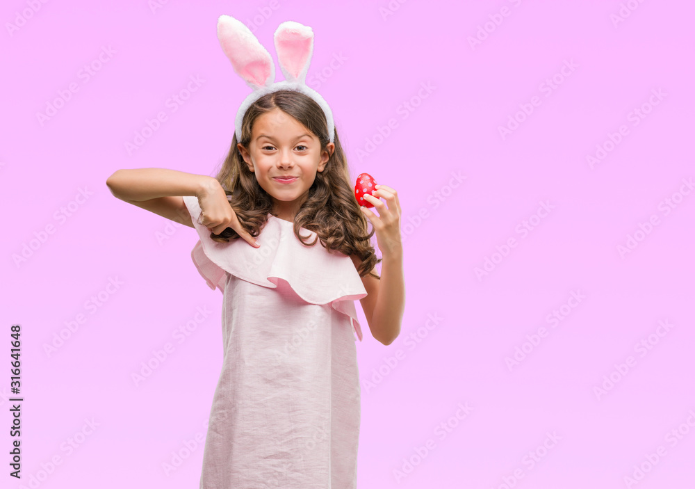 Brunette hispanic girl wearing easter rabbit ears with surprise face pointing finger to himself Brunette hispanic girl wearing easter rabbit ears with surprise face pointing finger to himself