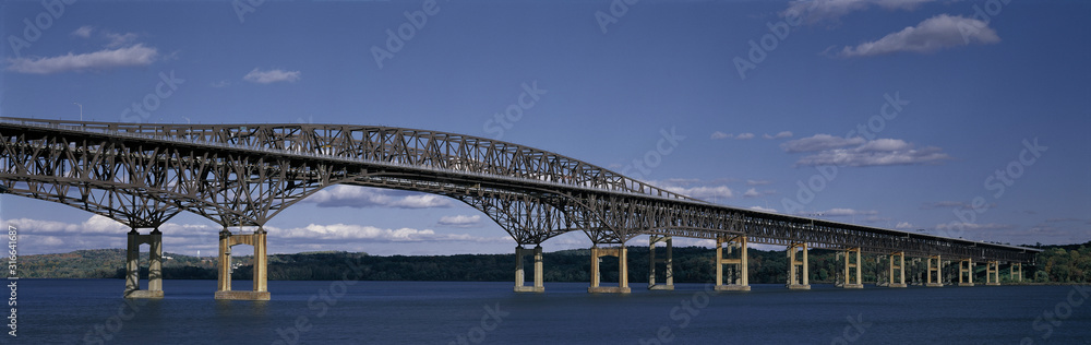 This is the Beacon Bridge which is over the Hudson River. It is a large steel bridge. The water and sky are blue. This is the Beacon Bridge which is over the Hudson River. It is a large steel bridge. The water and sky are blue.
