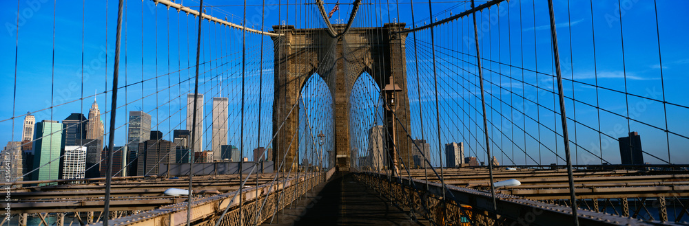 Obraz premium This is a close-up of the Brooklyn Bridge Walkway to Manhattan. The Manhattan skyline is in the background. The steel fencing is on either side of the bridge.