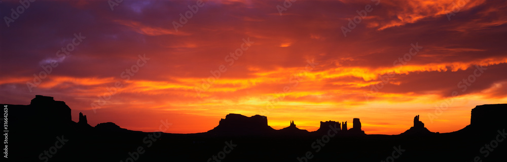 This is sunrise on Monument Valley. The rocks are in silhouette against an orange sky.