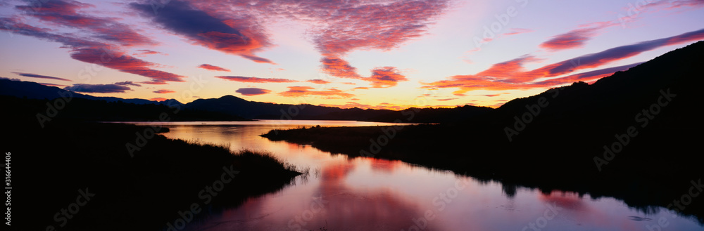 This is Lake Casitas at sunrise. There is a pinkish glow from the sun reflected in the lake.