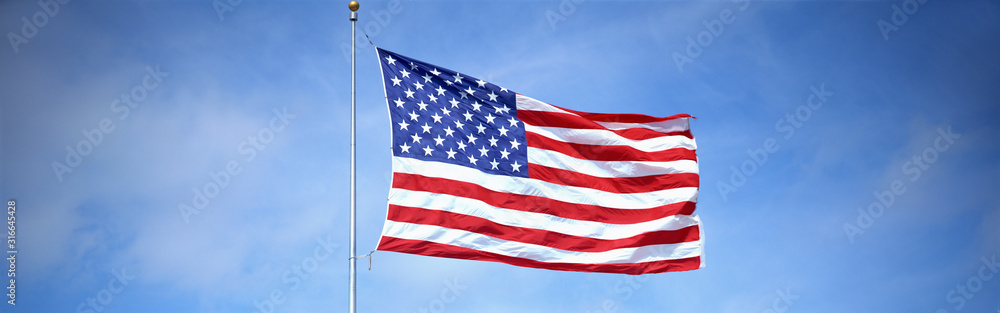 Obraz premium This is a shot of an American flag on a flagpole, waving in the wind against a blue sky.