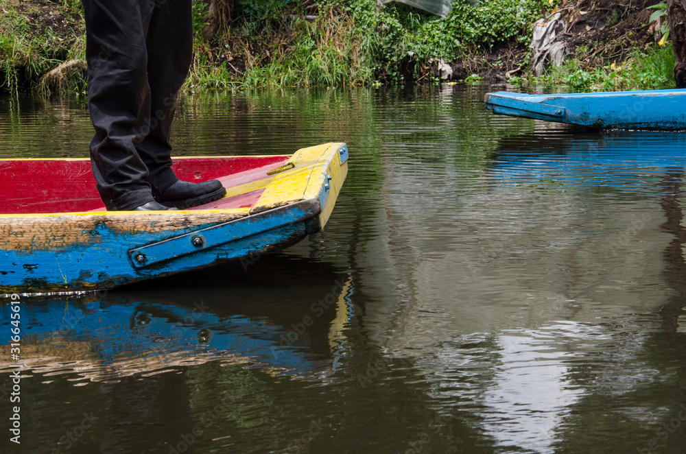 Xochimilco, Mexico; legs of a man at the end of a trajinera boat