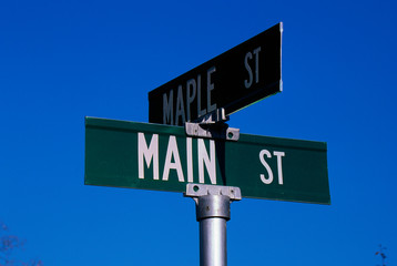 This is a street sign labeling the corner of Main Street & Maple Street. The sign is green with white lettering against a blue sky.