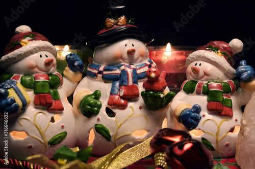 3 ceramic snowman with lit candles and Christmas bells in the foreground, on black background