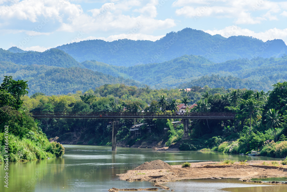 Obraz premium Scenic View of the Nam Khan River in Luang Prabang Laos with Hazy Cloudy Mountains in the Background