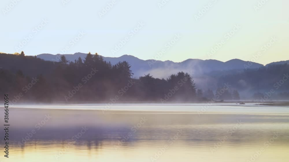 The yellow sun reflects on this early morning lake as the dark line of trees and hills offsets the background from the azure sky. The yellow sun reflects on this early morning lake as the dark line of trees and hills offsets the background from the azure sky.