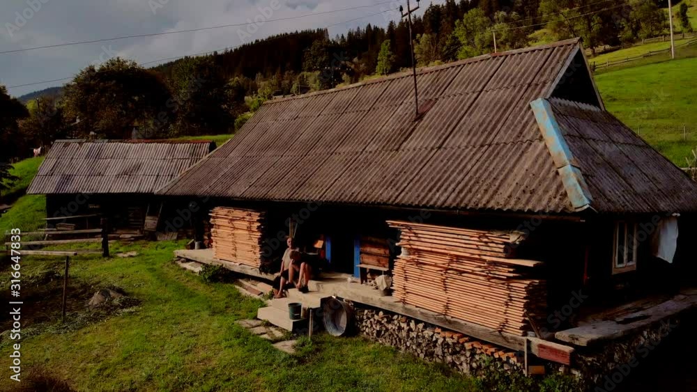 An old wooden hutsul house in Carpathian mountains. Two hutsuls at hut in summer. Beautiful landscape of the Ukrainian Carpathian village. An old wooden hutsul house in Carpathian mountains. Two hutsuls at hut in summer. Beautiful landscape of the Ukrainian Carpathian village.