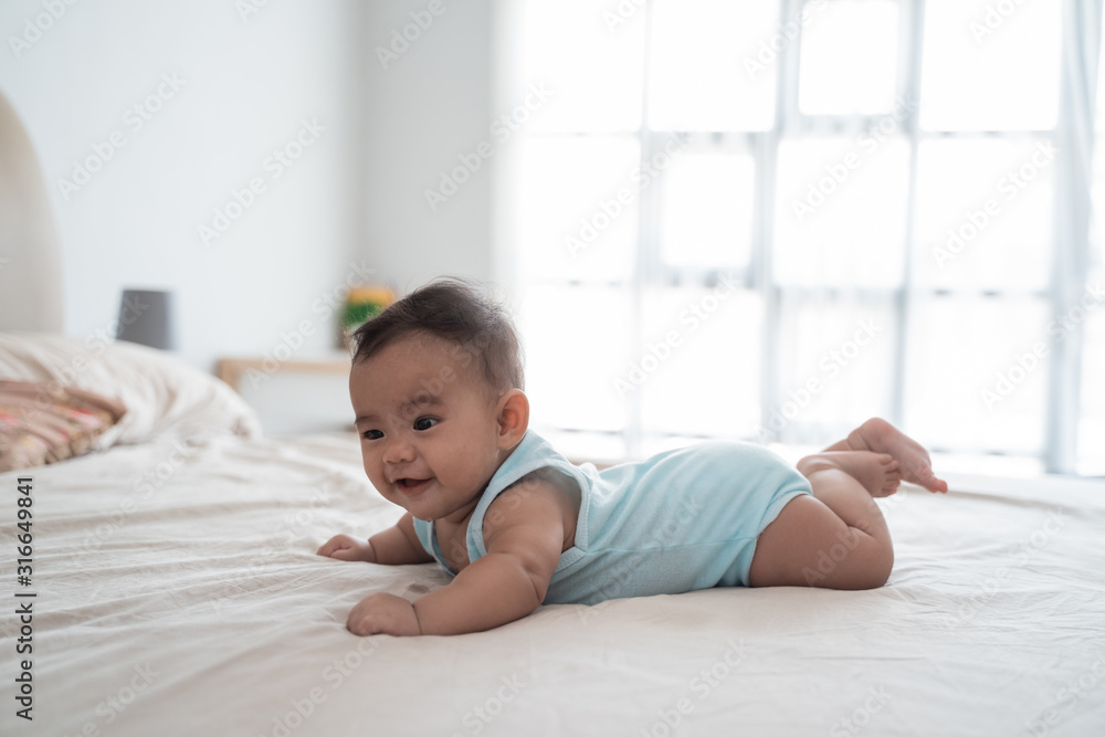 Cute happy 4 month baby lying on belly playing on the bed Cute happy 4 month baby lying on belly playing on the bed