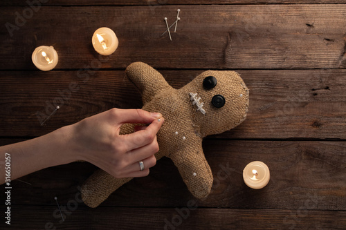 Voodoo doll on a wooden background with dramatic lighting and candles. The concept of witchcraft and black art. Burlap doll on a wooden background. Hands stick pins into a doll. Copy space.