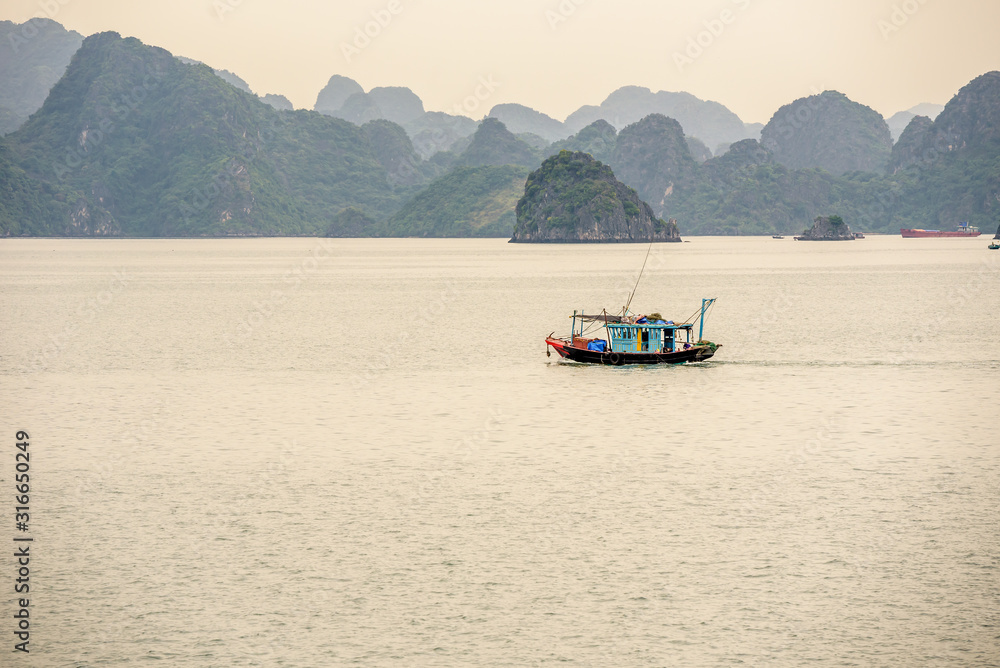 Traditional Vietnamese Fishing Boat Surrounded by Karst Mountains in Bai Tu Long Bay in Halong Bay Vietnam on a Cloudy Day