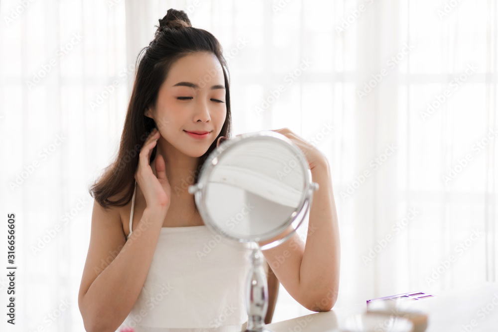 Smiling young beautiful asian woman fresh healthy skin looking on mirror with makeup cosmetics set at home.facial beauty and cosmetic concept Smiling young beautiful asian woman fresh healthy skin looking on mirror with makeup cosmetics set at home.facial beauty and cosmetic concept