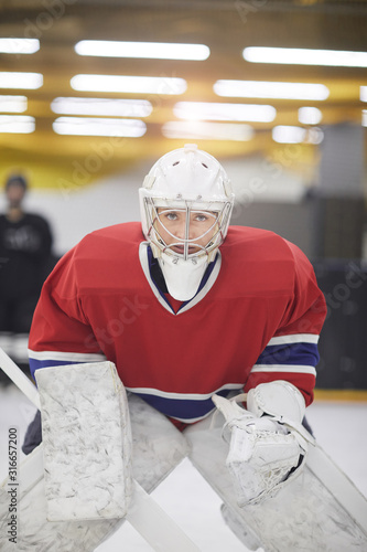 Portrait of determined female hockey player in full gear looking at camera while ready to defend team during match