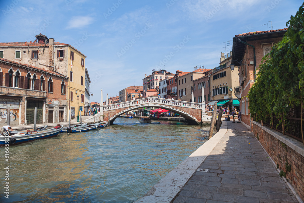 VENICE, ITALY - JUNE 15, 2016 View of the Ponte delle Guglie (Bridge of Spires) over the Canaregio Canal on a bright sunny day. A crowd of tourists on the bridge.
