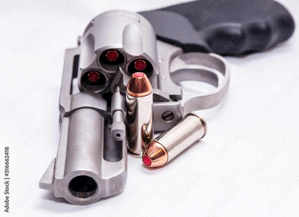 A loaded 44spl stainless steel revolver with two hollow point bullets next to it on a white background