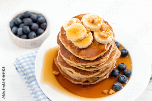 Pancakes with banana, blueberry, crushed walnut and caramel syrup on a white plate, closeup view. Tasty sweet breakfast food