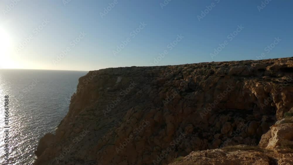 Camera reveals beautiful bright sun right next to a rocky cliff. Beautiful view of the Mediterranean Sea. Cap de Barbaria, Formentera, Spain. Slow motion. Camera reveals beautiful bright sun right next to a rocky cliff. Beautiful view of the Mediterranean Sea. Cap de Barbaria, Formentera, Spain. Slow motion.