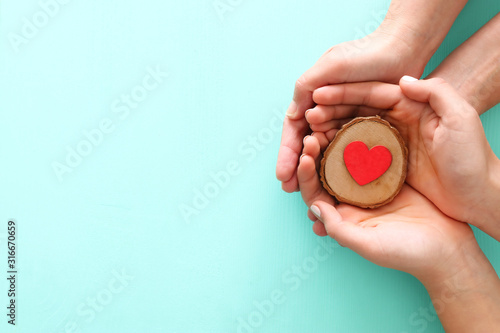 Valentine's, father's and mother's day background. Little child with mother heands holding red heart . Top view photo