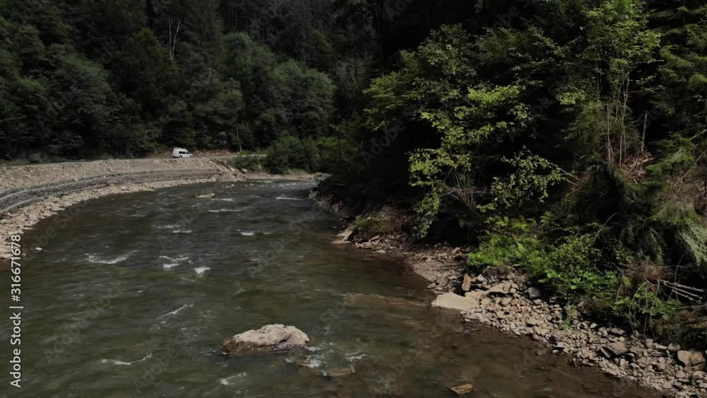 Mountain river flowing through the green forest. Landscape with mountain river flowing near road on forest background. Mountain river flowing through the green forest. Landscape with mountain river flowing near road on forest background.