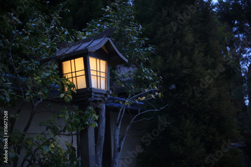 Japanese style garden lamp. Japanese gable roof house light post in traditional garden. warm light in cool sunset garden.