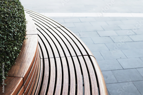 Peaceful outdoor summer image of wooden rounded bench with flowerbed in center on blue floor tiles and white strip line.Image use for imply loneliness in big city.