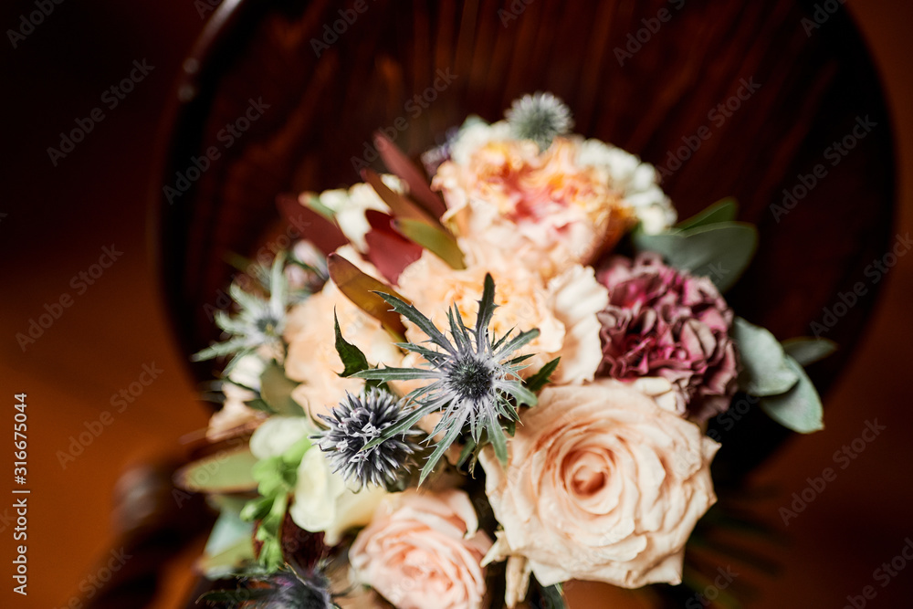 The bride’s wedding bouquet of natural roses and other plants lies on a wooden chair.